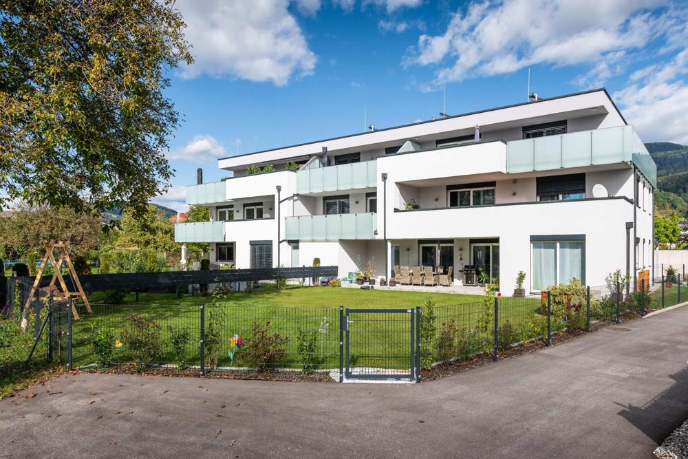 Dreigeschoßige weiße Wohnanlage mit Flachdach, Glasbalkonen und eingezäunten Gärten