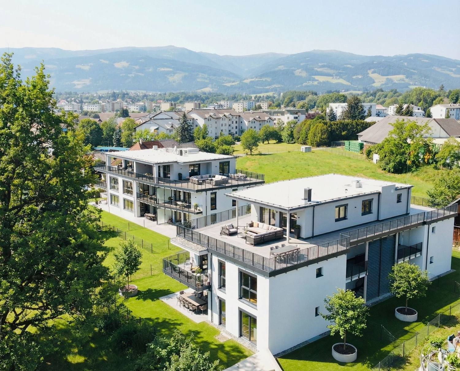 Zwei weiße Wohngebäude mit Dachterrassen, Luftaufnahme vor Bergkulisse