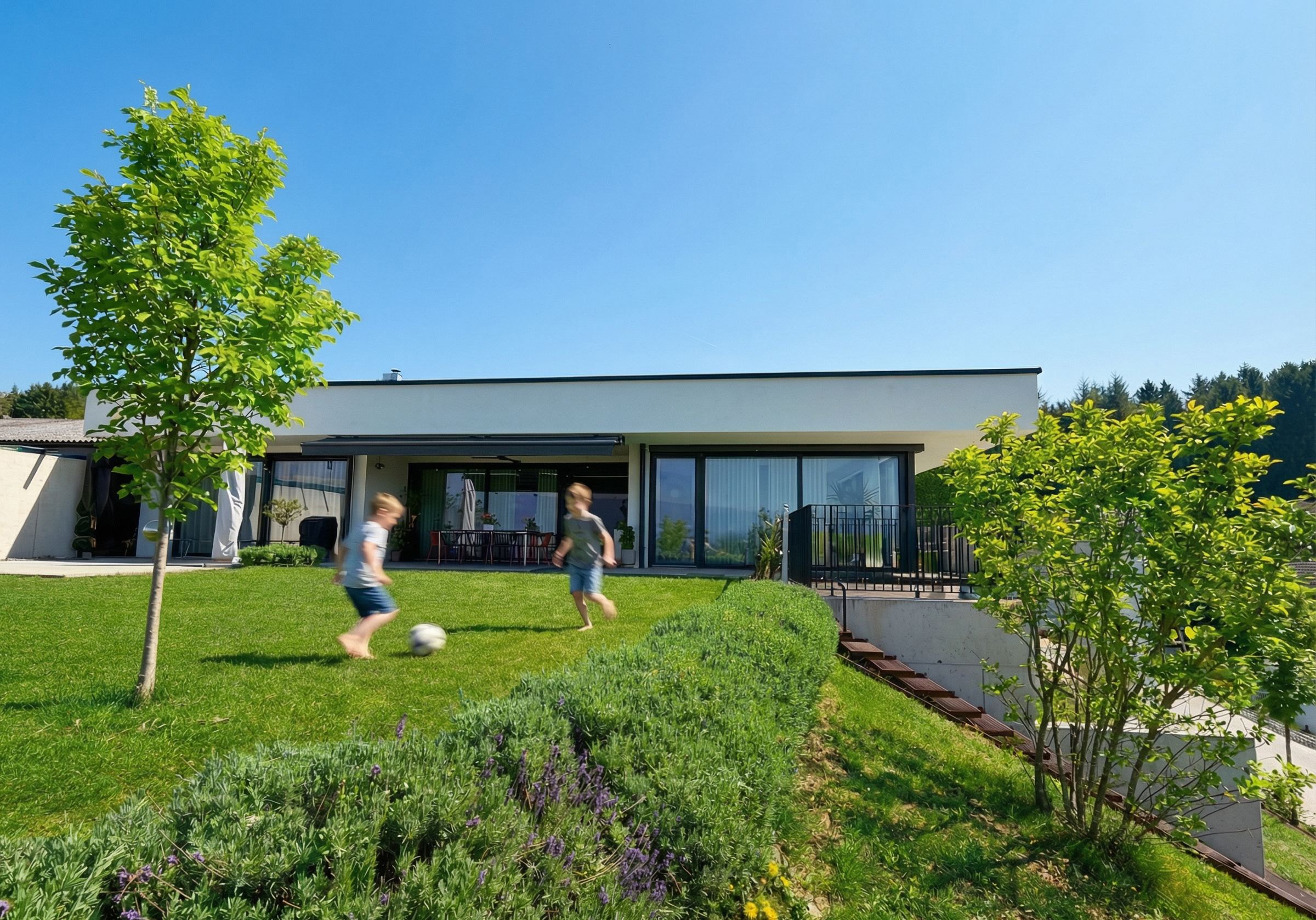 Eingeschoßiges Wohnhaus mit Flachdach und großen Glasflächen, davor Garten am Hang